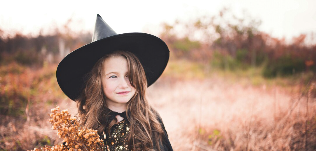 Girl wearing a black witch costume holding a brown plant in a field