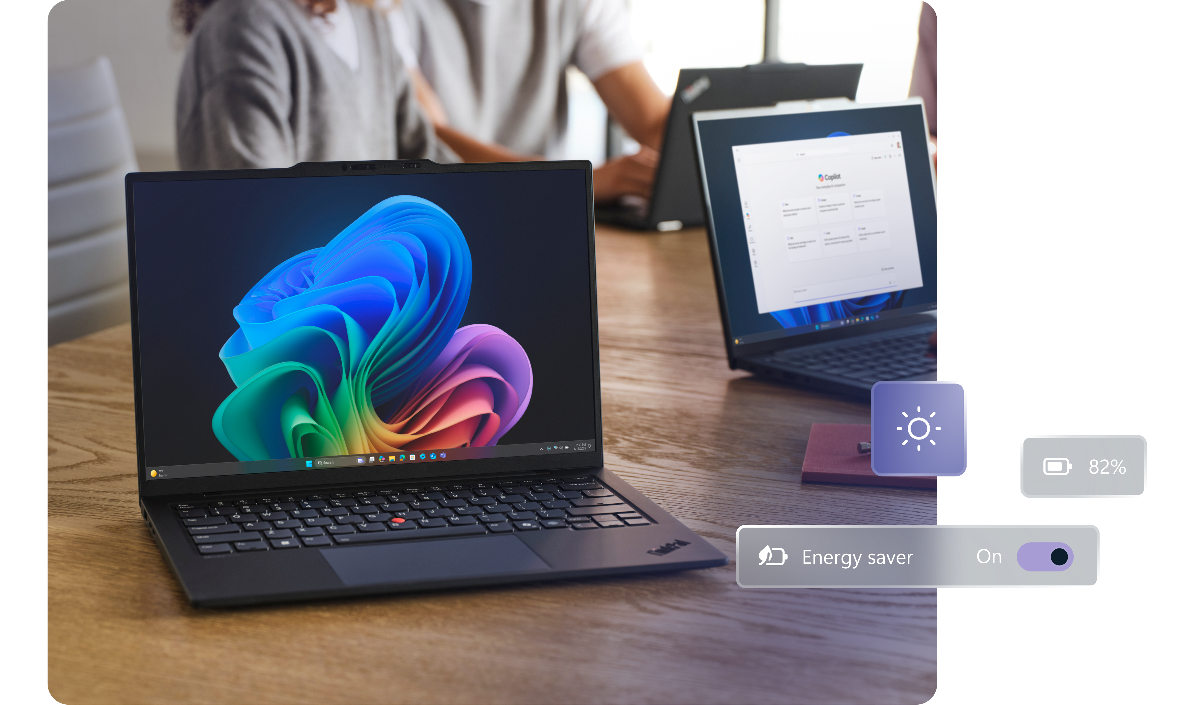 A large worktable with three open laptops, one facing forward displaying the rainbow bloom image, with two people working in the background, and conceptual images showing energy use and battery level