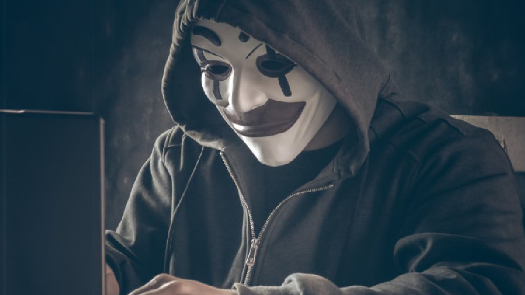 Image of a suspicious person wearing a mask and hacking into a device