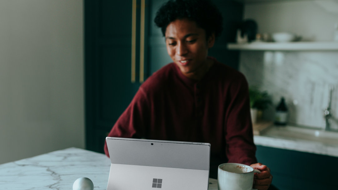 Image of a man sitting at a kitchen table, drinking coffee, and happy using a Surface, Copilot+ PC