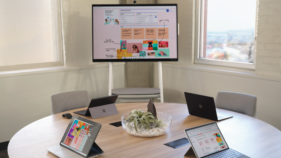 Laptops around a circular table and a TV monitor displaying a presentation