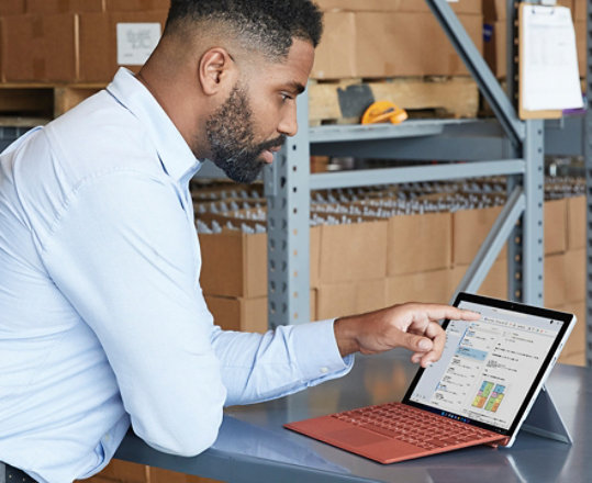 Muž na videohovoru Microsoft Teams ve skladu. Použité zařízení je platinový Surface Pro 7+ v režimu přenosného počítače.