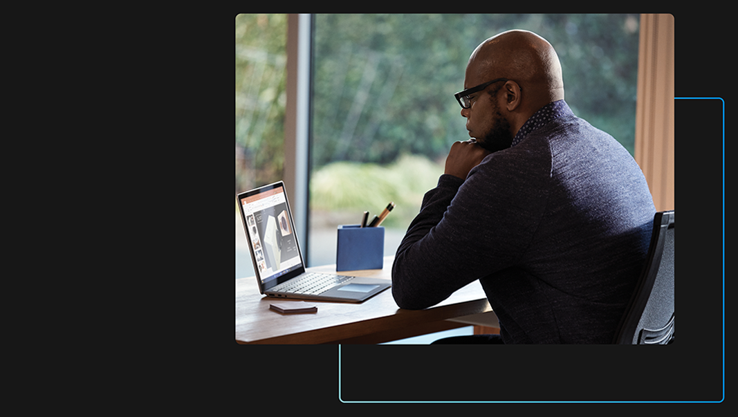 Man at desk and working on laptop with PowerPoint presentation on screen.
