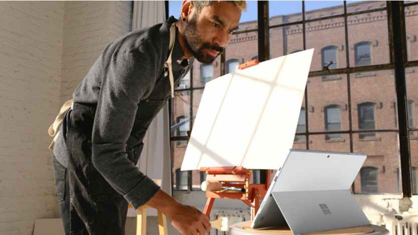 Man looking at Surface device while standing in front of a canvas