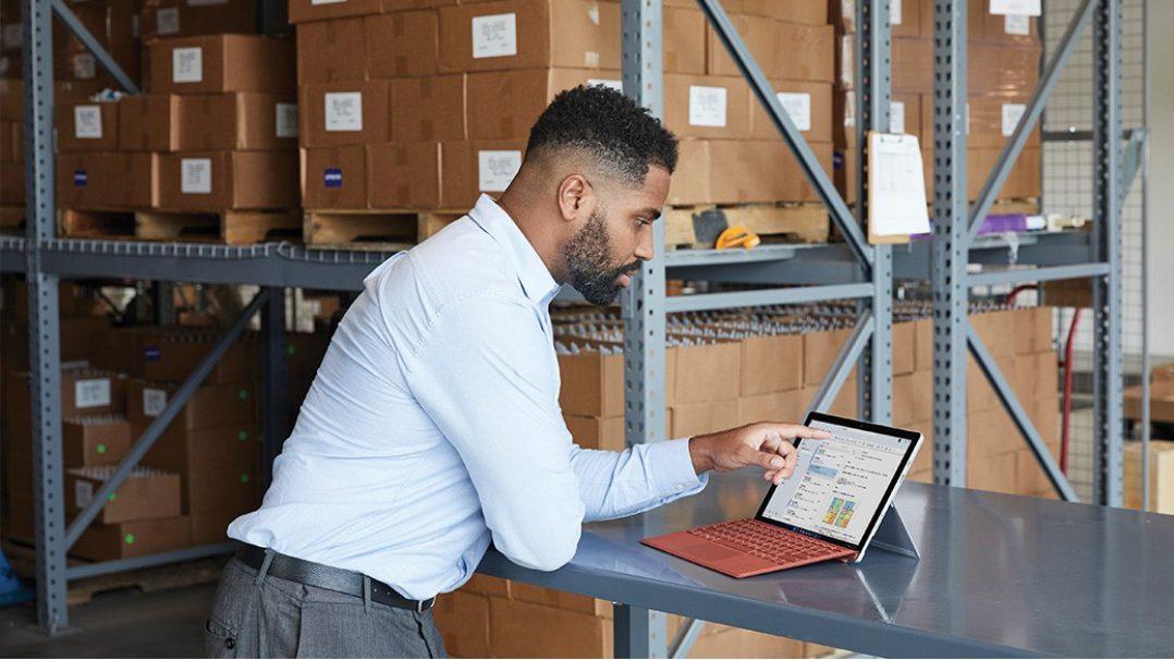 一名男子在仓库环境中进行 Microsoft Teams 视频通话。使用的设备是便携式计算机模式的亮铂金颜色的 Surface Pro 7+。