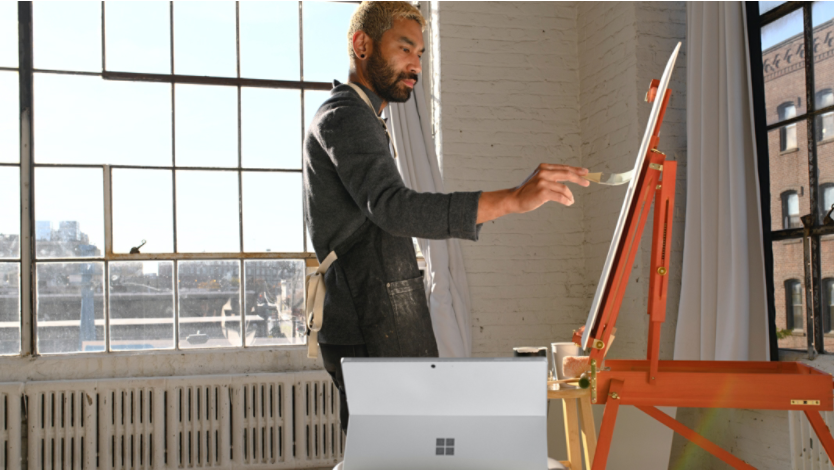 Man painting on easel in artist loft with Surface laptop