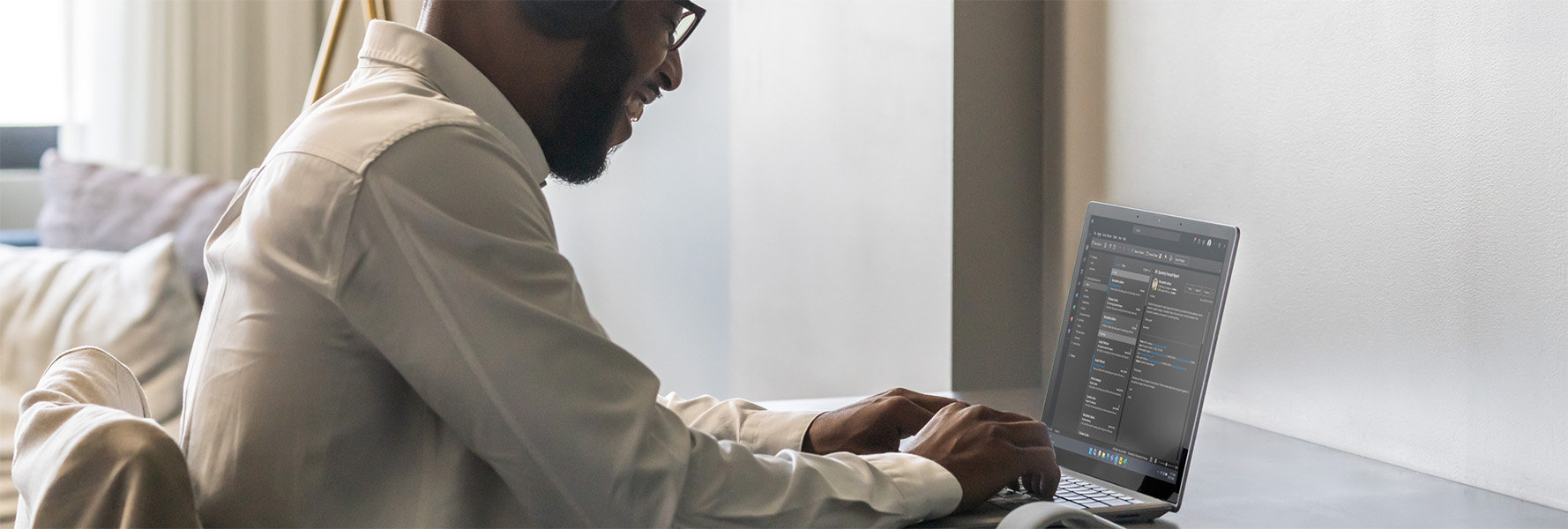 Man zittend aan een bureau, lachend en typend op zijn Surface-apparaat