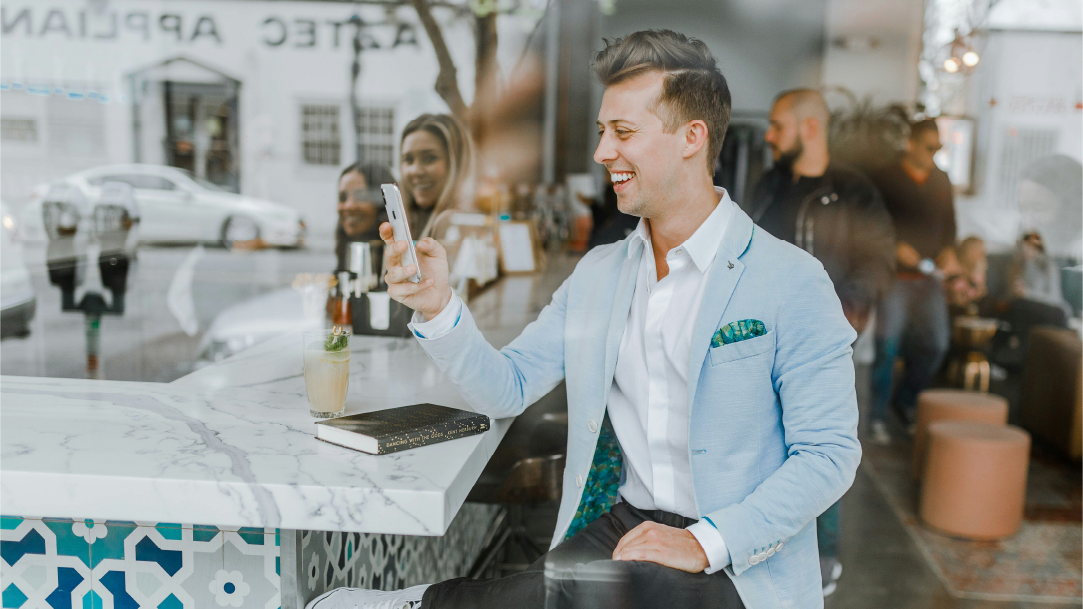 Man sitting in a café wearing a blue suit smiling while holding a smartphone