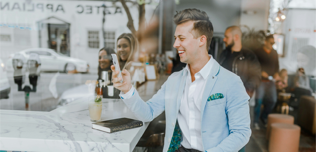 Man sitting in a café wearing a blue suit smiling while holding a smartphone