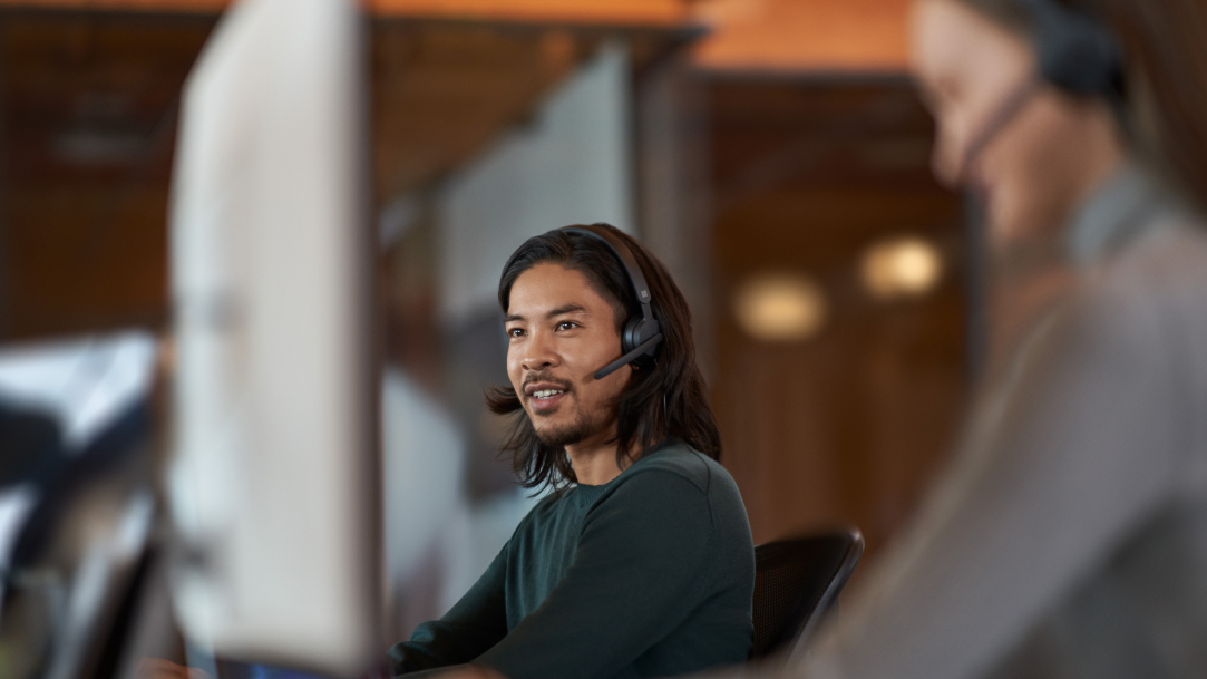 Man sitting next to coworker while on a computer listening to headphones