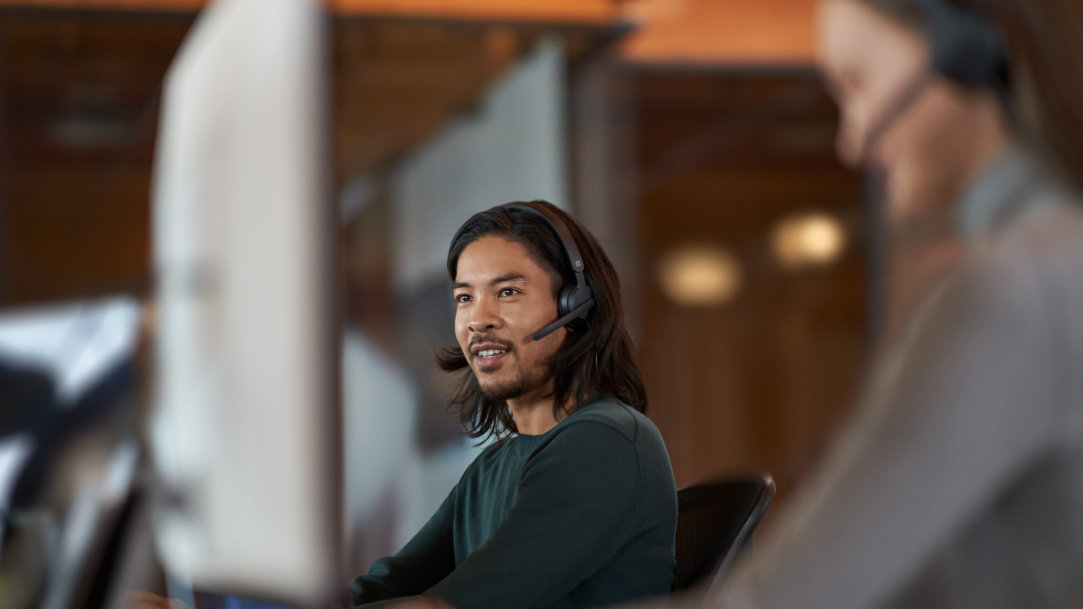 Man sitting next to coworker while on a computer listening to headphones