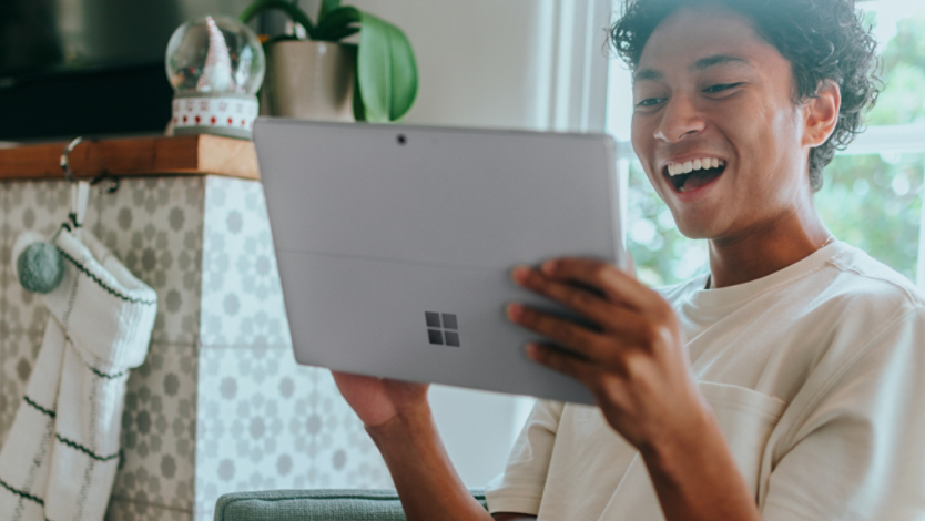 Man smiles while holding a Microsoft Surface 2-in-1 PC