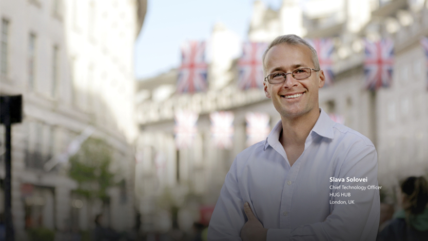 Person smiling in front of buildings displaying UK flags