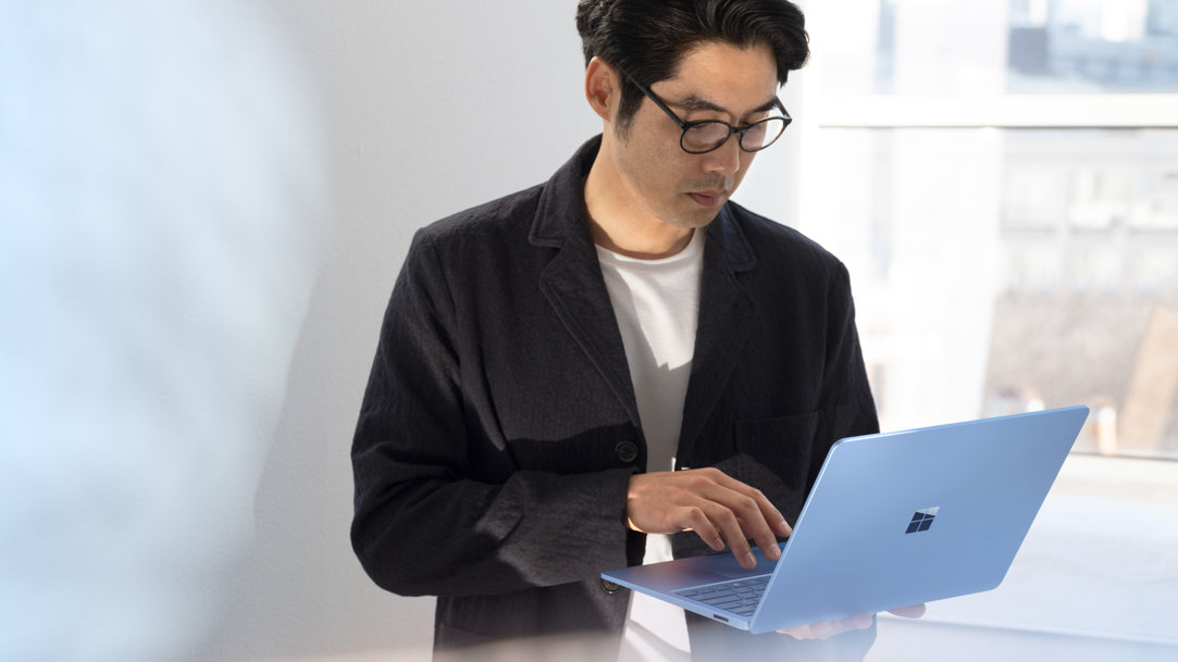 Man standing up holding his Surface Laptop 7ᵗʰ Edition