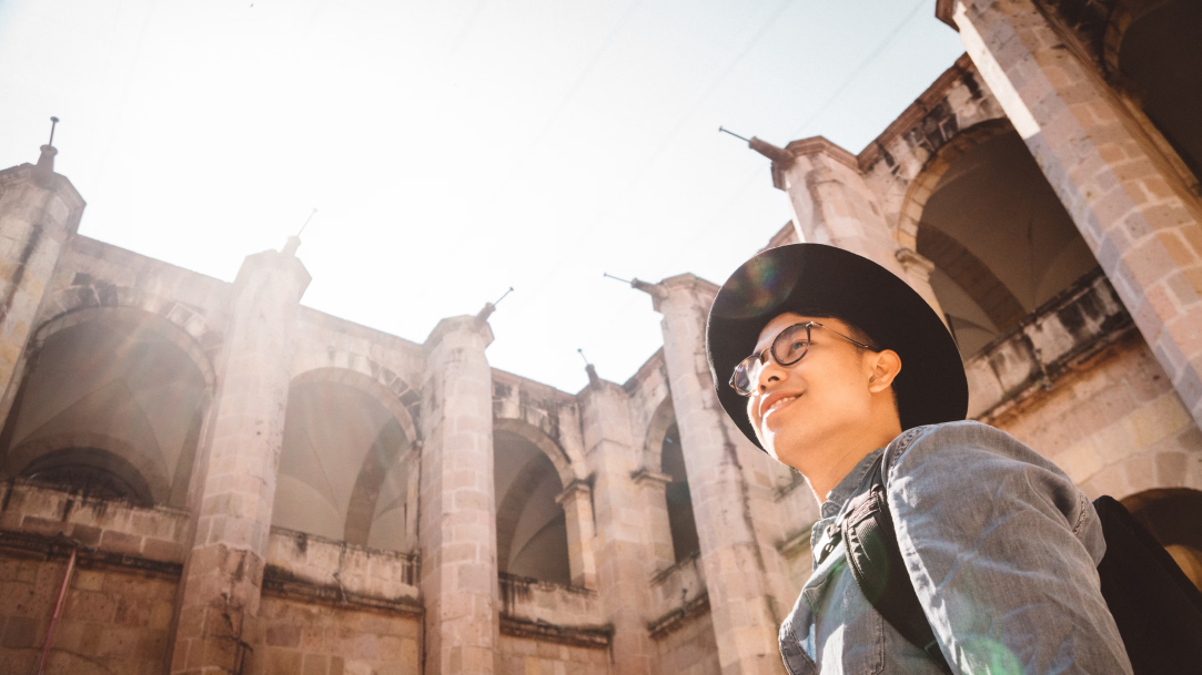 Man wearing a hat and glasses smiles while looking at a building