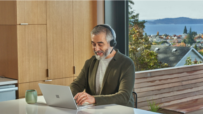 A man works from his kitchen table with a headset on