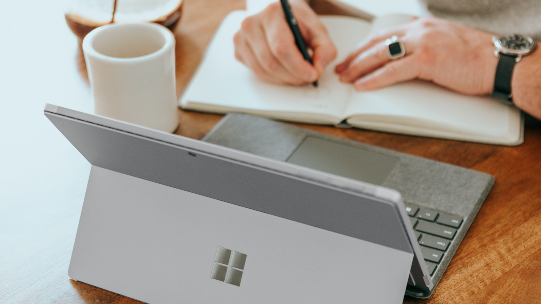 Man writing in a notebook in front of a Surface device