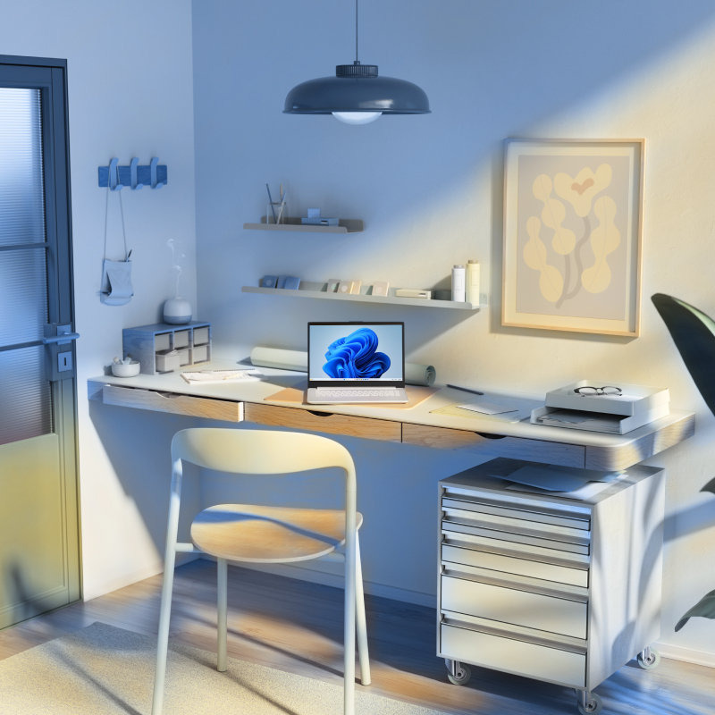 An open laptop with a blue bloom screen sitting on a desk with a chair, drawers, shelves, framed picture, and pendant light.