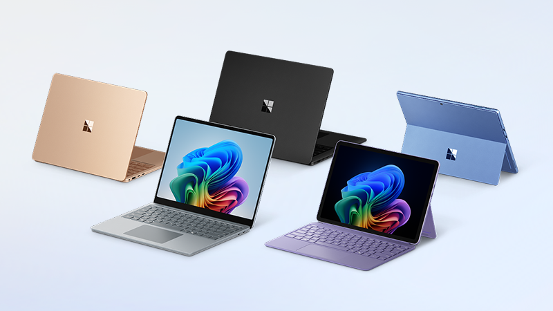 Several Surface devices in different colors, two with the Windows colorful bloom on the screen