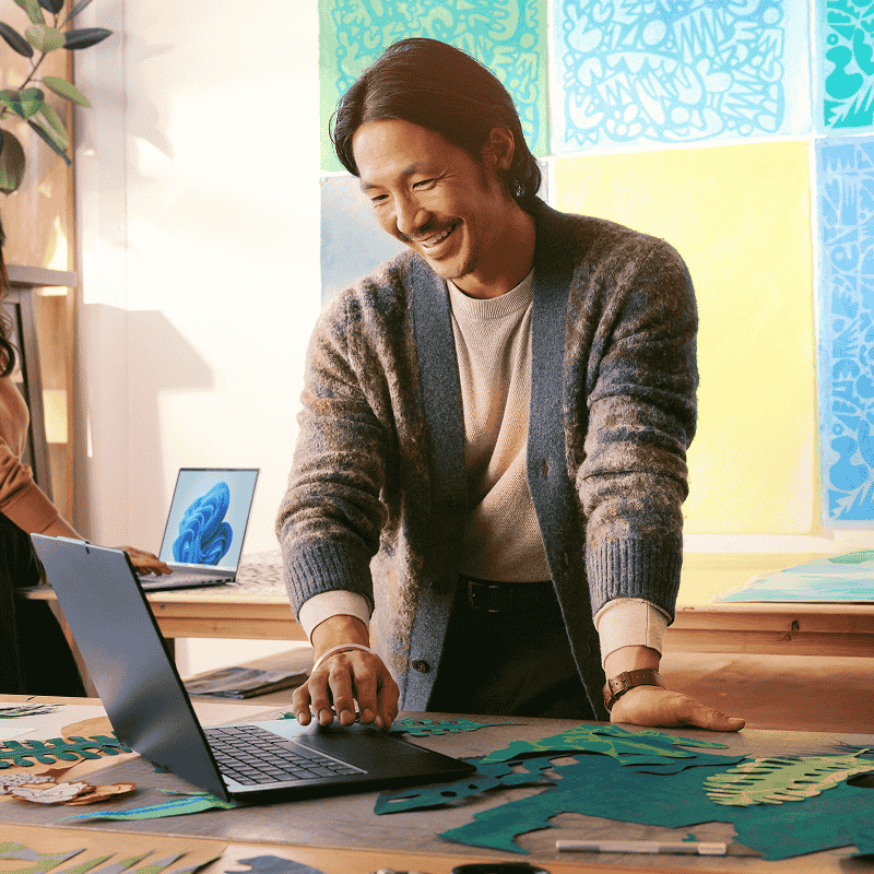  一位面带微笑的女士正在一台打开的笔记本电脑上打字，电脑屏幕上放大显示着 PowerPoint 应用，还有“回顾”搜索栏以及“回顾”徽标，背景为浅橙色