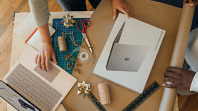 Overhead view of a person with a laptop box and gift-wrapping material, while also using a laptop