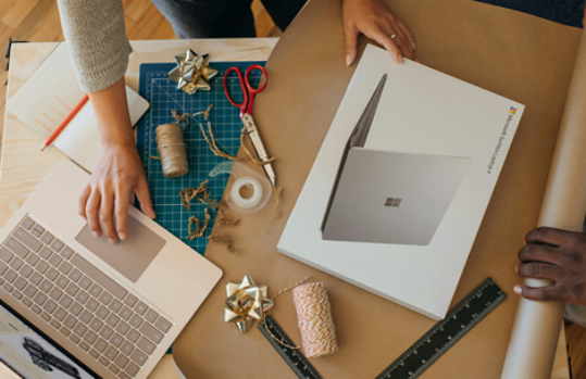 Overhead view of a person with a laptop box and gift-wrapping material, while also using a laptop