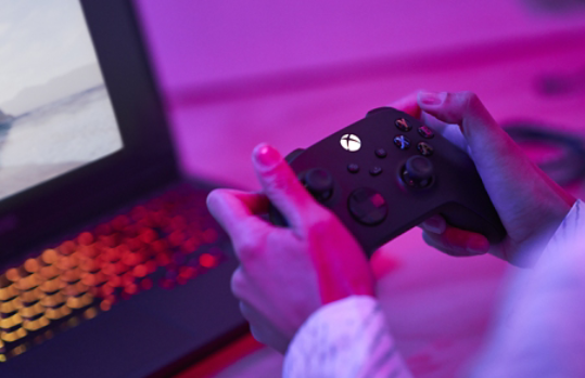 Person som håller i en spelkontroll med en bärbar dator i bakgrunden