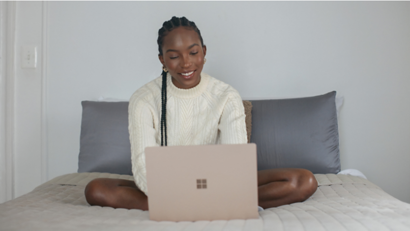 Person in white shirt on bed using Surface laptop