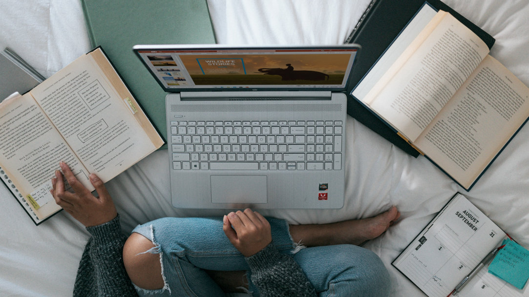 Person sitting on a bed with computer and books laying around her