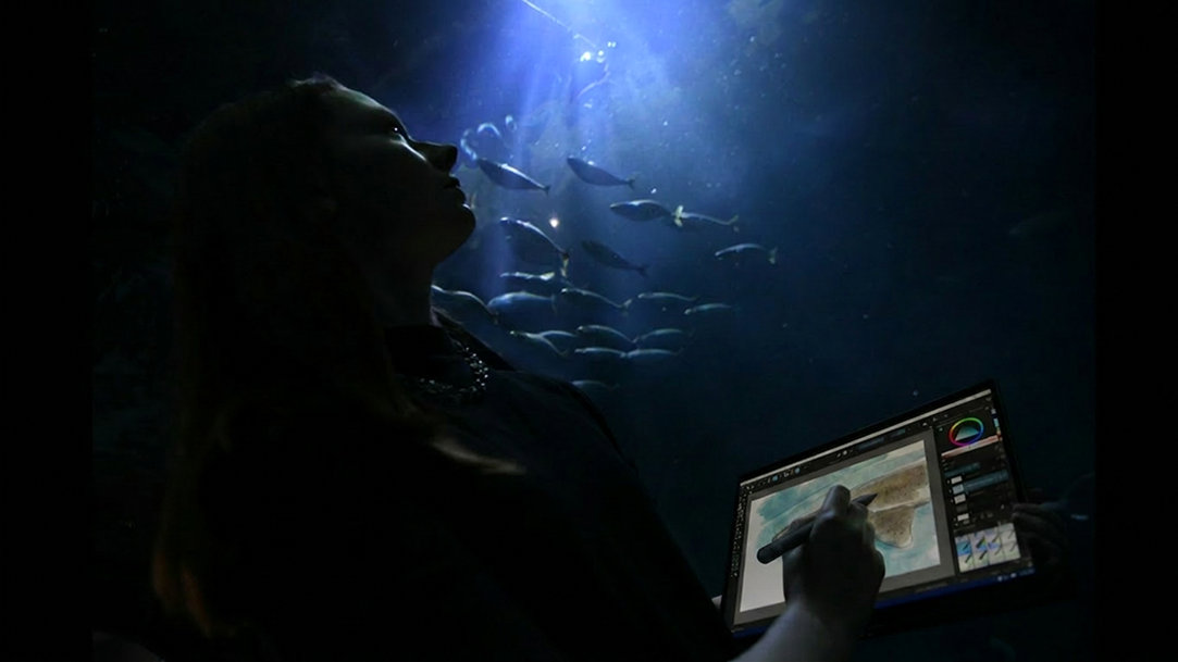 Person sketching on a Surface Pro in an aquarium as fish swim overhead