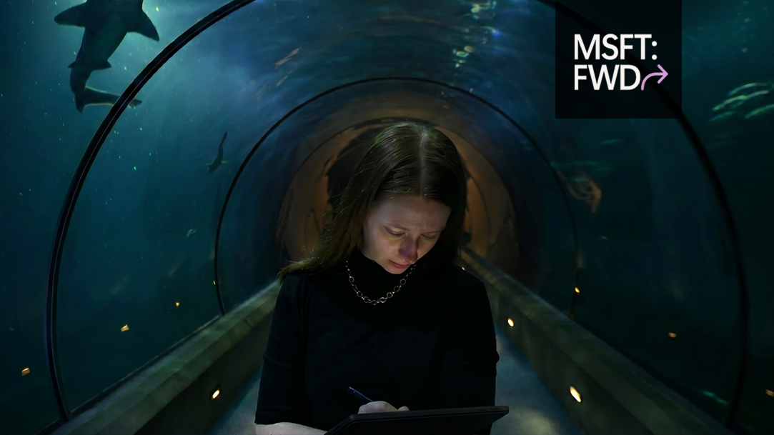 Person sketching on a Surface Pro in an aquarium as whale sharks swim overhead