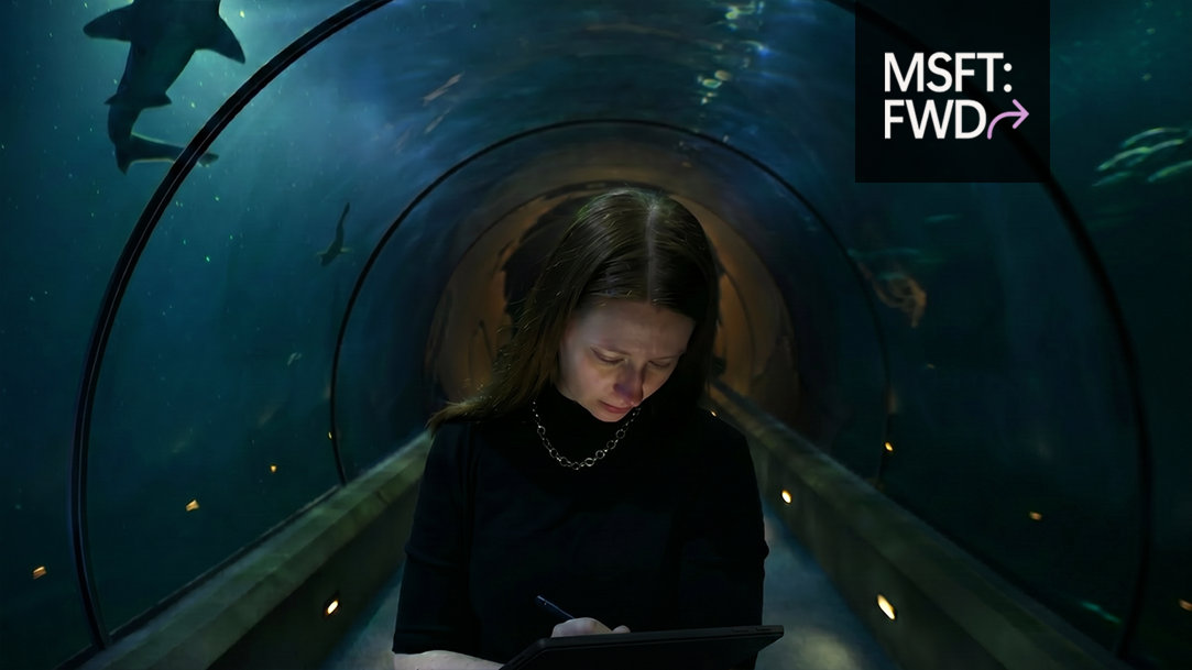 Person sketching on a Surface Pro in an aquarium as whale sharks swim overhead