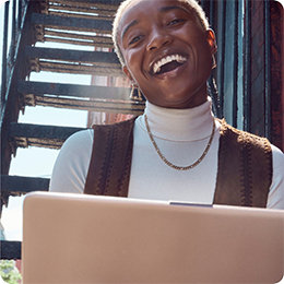 Fehér inget és barna mellényt viselő, mosolygó személy, kezében egy számítógéppel.