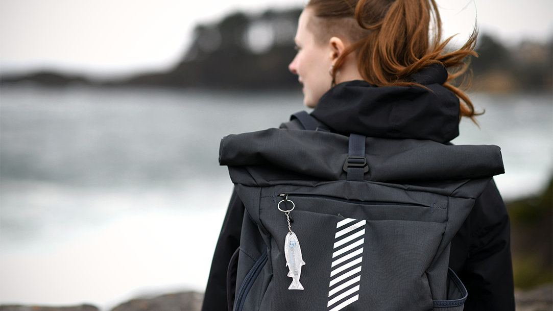 Person with a backpack standing near the ocean on a rocky shoreline