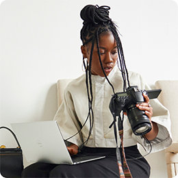 Person med långa flätor som håller i en dator och en kamera