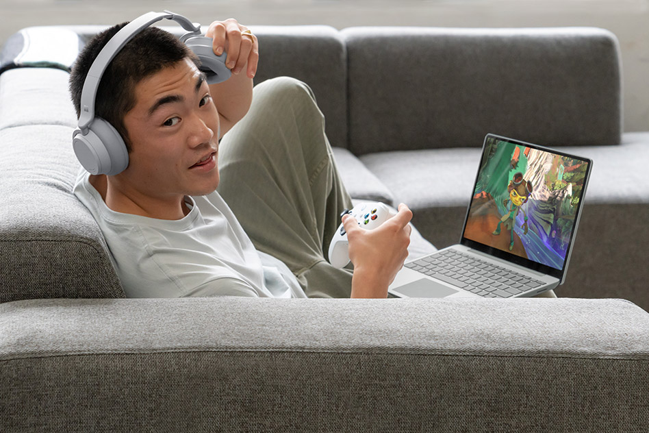 A man plays Xbox games on his Surface Laptop Go 2 while sitting on the couch.