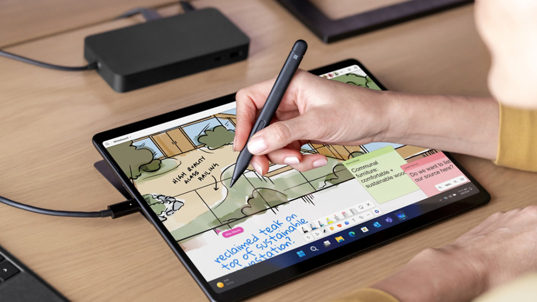 A person's hand is observed using Surface Slim Pen 2 on the screen of Surface Pro 8 with Surface Pro Signature Keyboard next to it