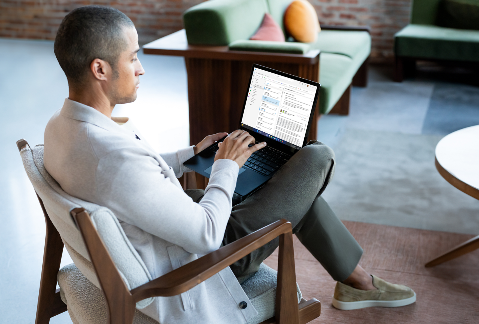 Un uomo seduto su una sedia con un computer Surface Laptop 6 sulle gambe