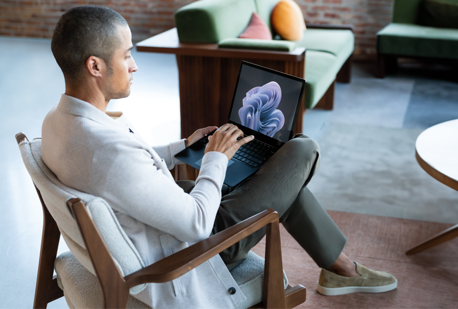 男人坐在椅子上，腿上放着 Surface Laptop 6