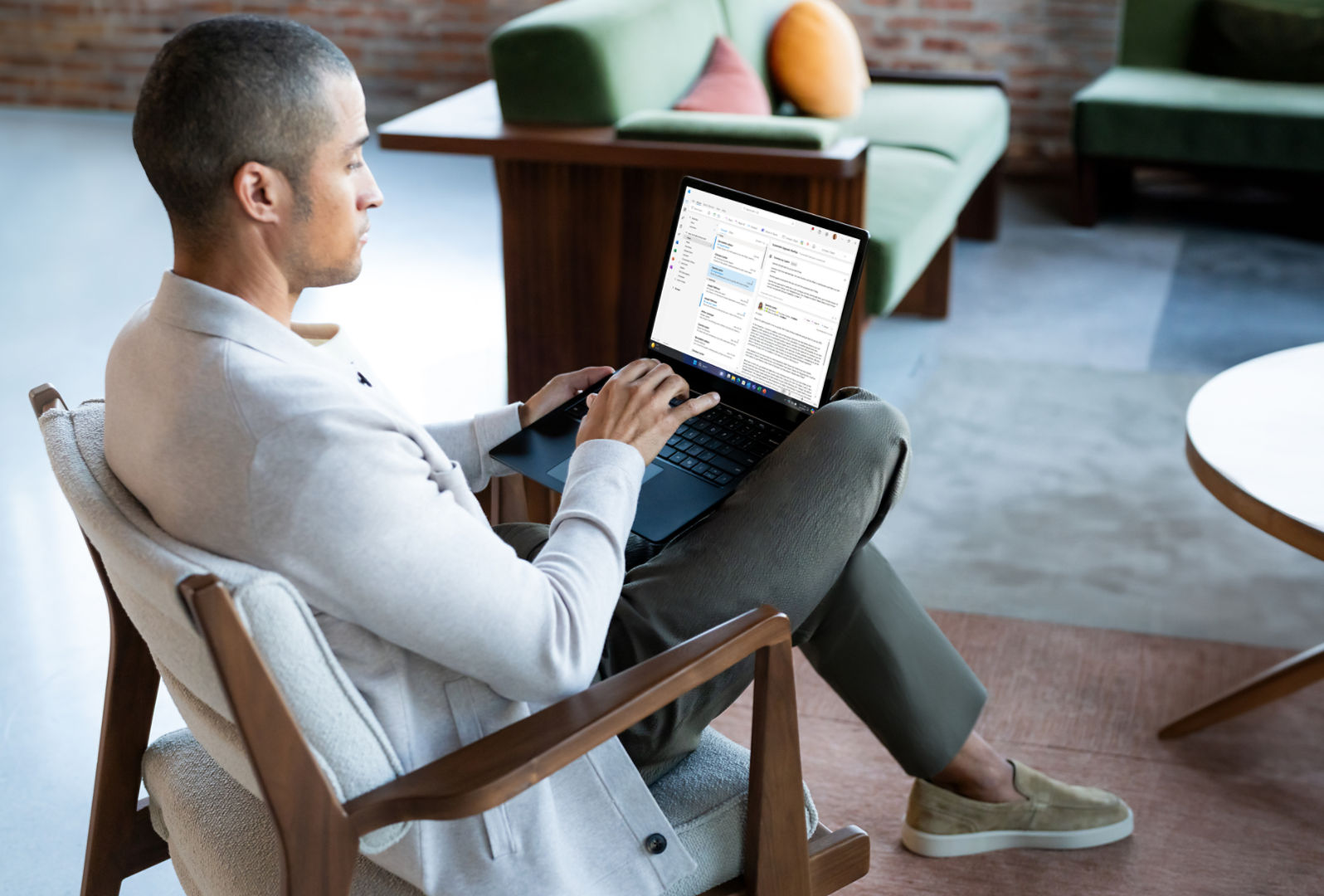 一名男性坐在椅子上，腿上放著 Surface Laptop 6