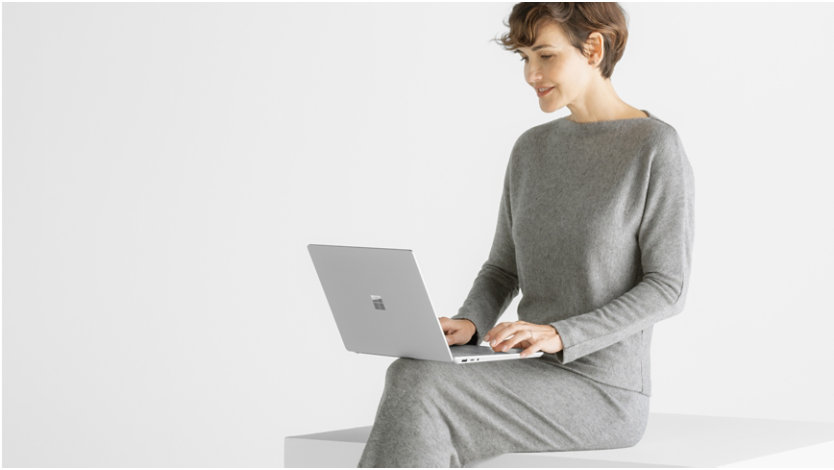 O femeie așezată pe un scaun, cu laptopul Surface Laptop 6 în poală