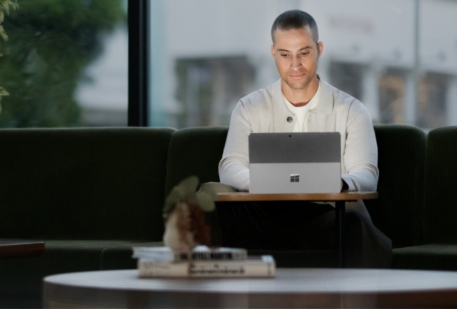 작은 탁자 앞에서 일하는 남성과 노트북 모드의 Surface Pro 10 제품을 보여 주는 이미지