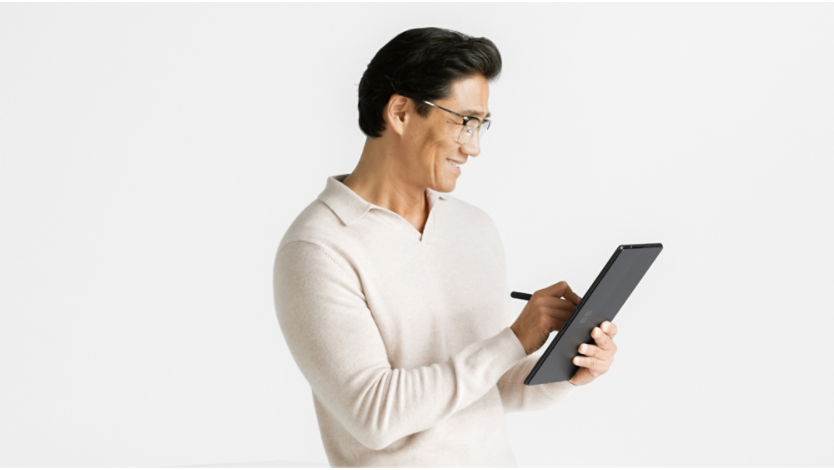 Un bărbat stând așezat și ținând în mână dispozitivul Surface Pro 10 în modul tabletă