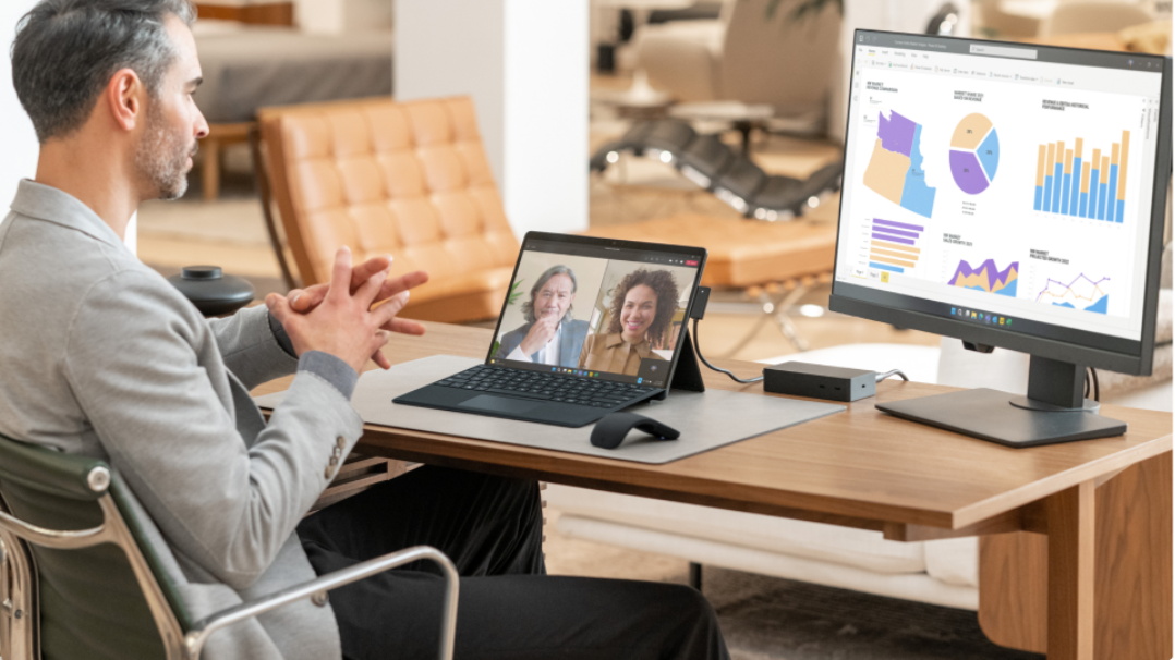 A man sits at his desk and uses a Surface computer to converse with teammates on an online video call