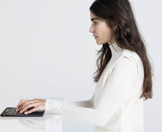 Surface Pro 디바이스를 키보드에서 분리하여 스탠드에 놓은 상태로 책상 앞에 앉아 키보드 입력을 하는 여성의 이미지.