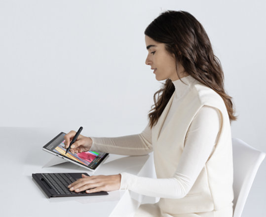 O femeie care stă la masă, cu dispozitivul Surface Pro în modul de suport rabatabil, în timp ce lucrează. 