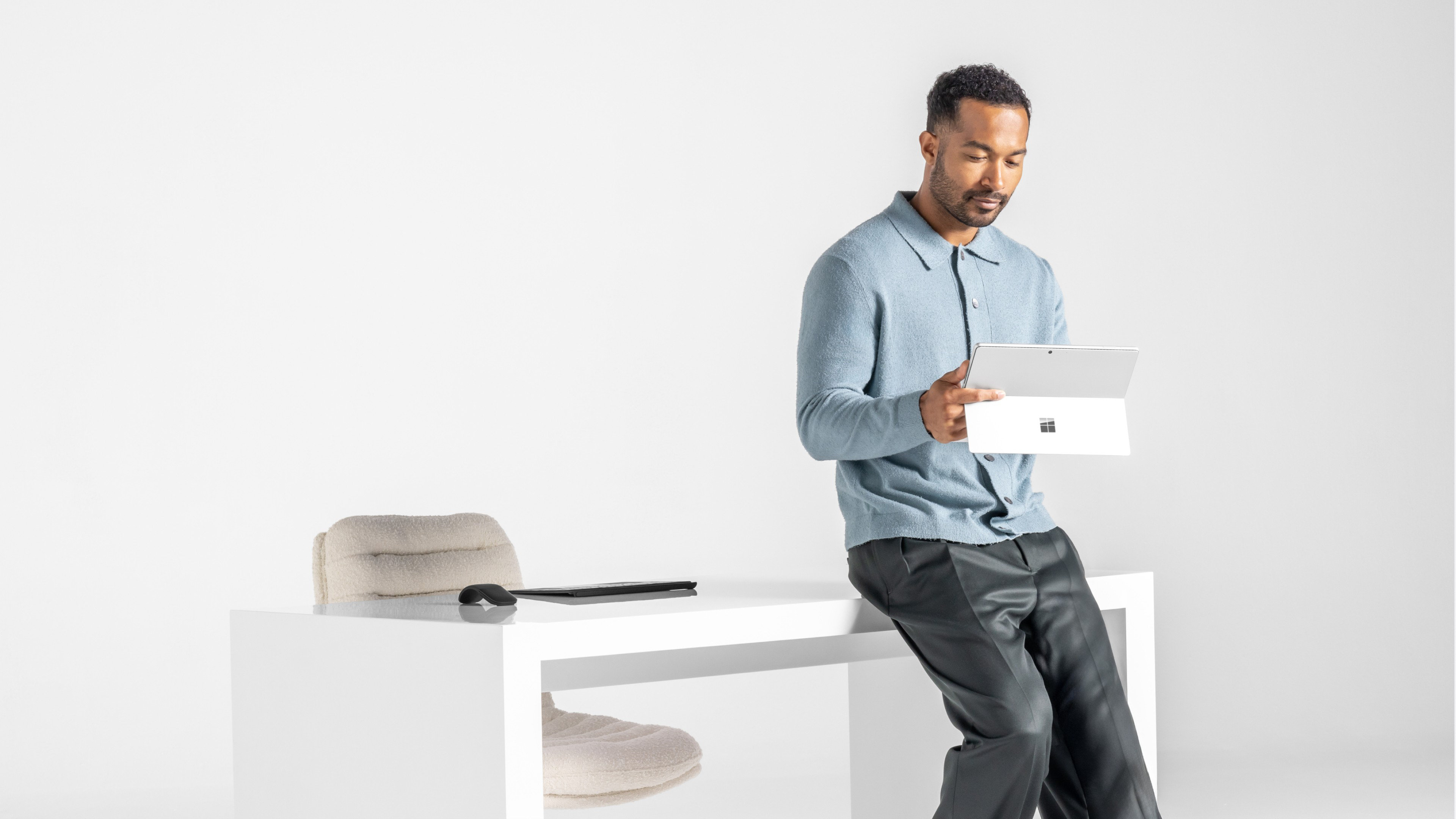 A man leaning up against his desk using a Surface device