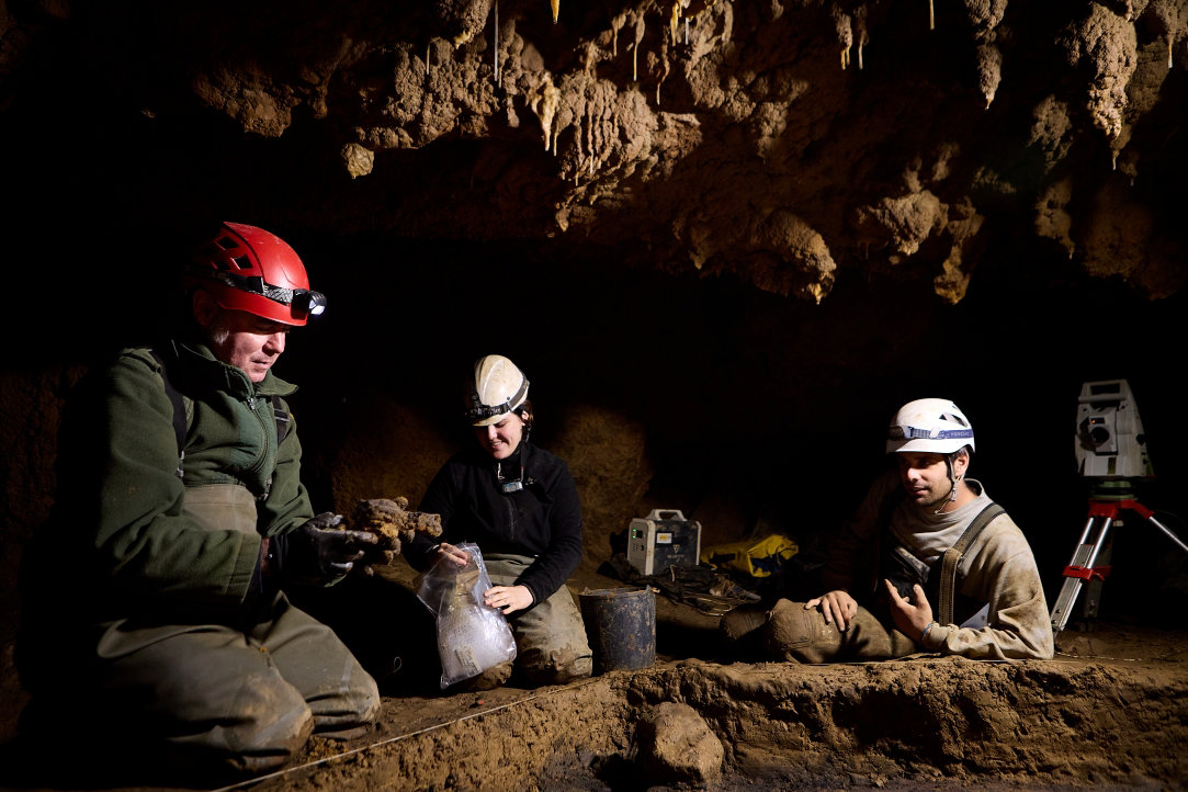 Three archeologists study specimens inside a remote Spanish cave