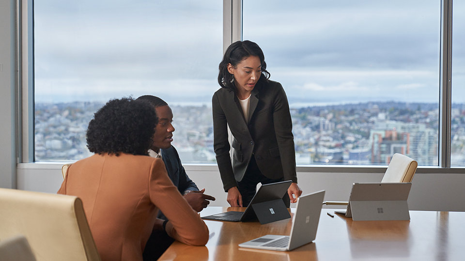 Three coworkers are observed in an office setting. Surface Pro and Laptop Go 2 devices are on the conference table