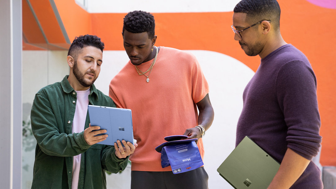 Three men sharing two colorful Surface devices